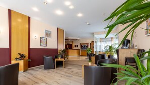 A modern hotel lobby with wooden flooring, black leather seating, and a reception desk. - Fly Inn Hotel Frankfurt Airport Rüsselsheim ehemals Trip Inn Hotels (Ruesselsheim)