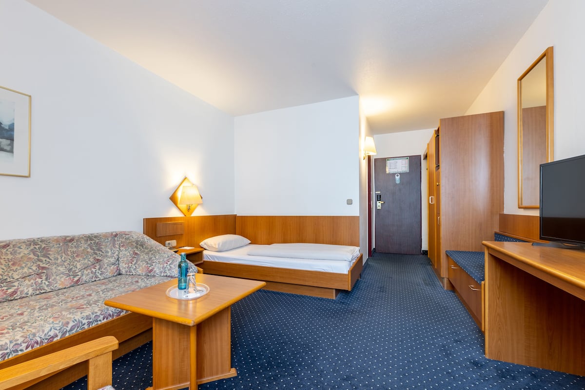A hotel room with a bed, a sofa, a desk, a TV, and a lamp.