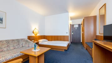 Quarto de hotel com cama, sofá, escrivaninha, televisão e luminária.