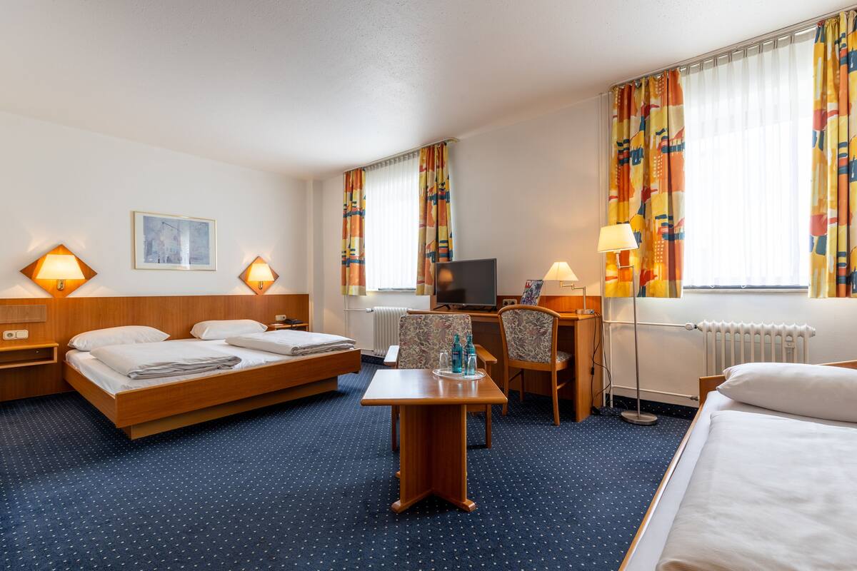 A hotel room with a bed, a desk, a chair, a TV, and a window with curtains.