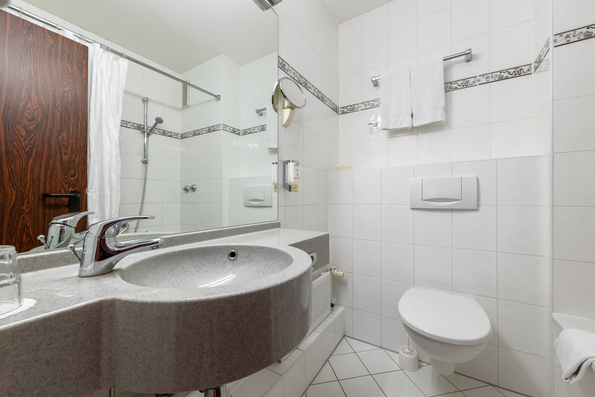 A modern bathroom with a granite sink, a mirror, a shower, and a toilet.