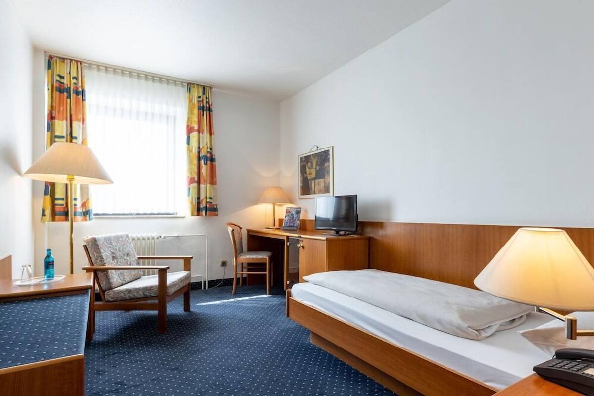 A hotel room with a bed, desk, chair, TV, and a window with curtains.