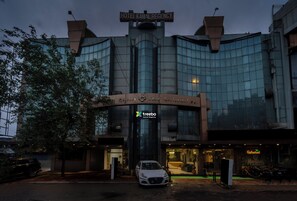 Een hotel met een moderne glazen gevel, een bord waarop 'Hotel Kamal Regency' staat en een 'treebo' logo.