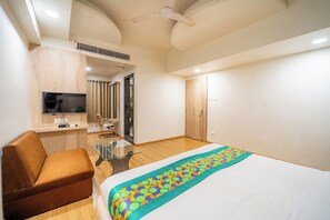 Hotelkamer met een bed, een bank, een televisie, een plafondventilator en een deur.