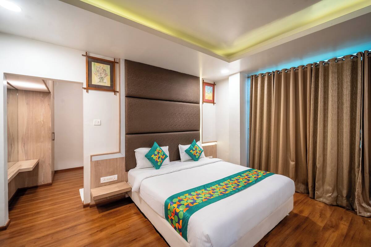 A modern hotel room with a large bed, wooden flooring, a headboard, and a view of the outside.
