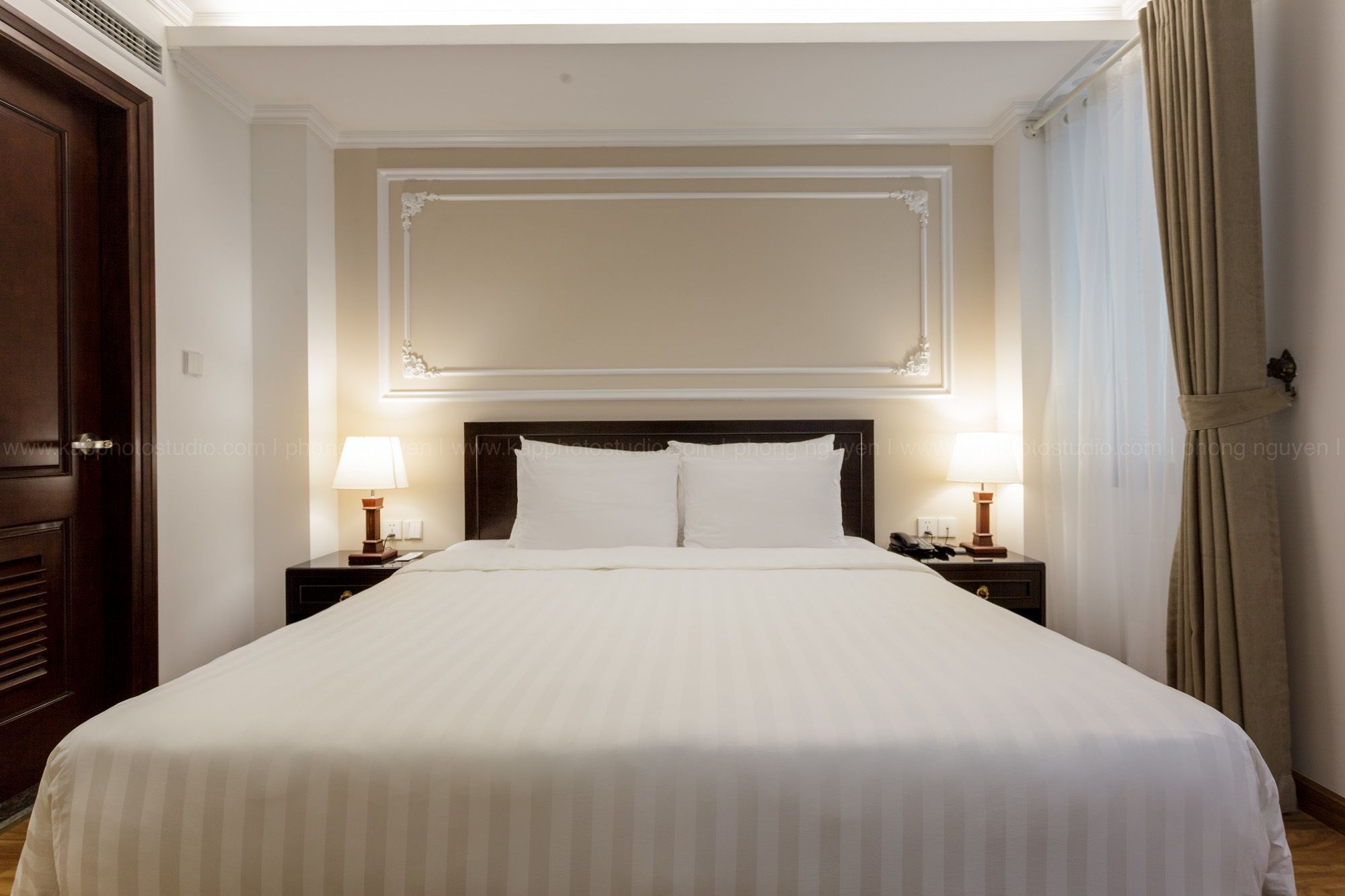 A hotel room with a large bed, two bedside lamps, and a wooden headboard.