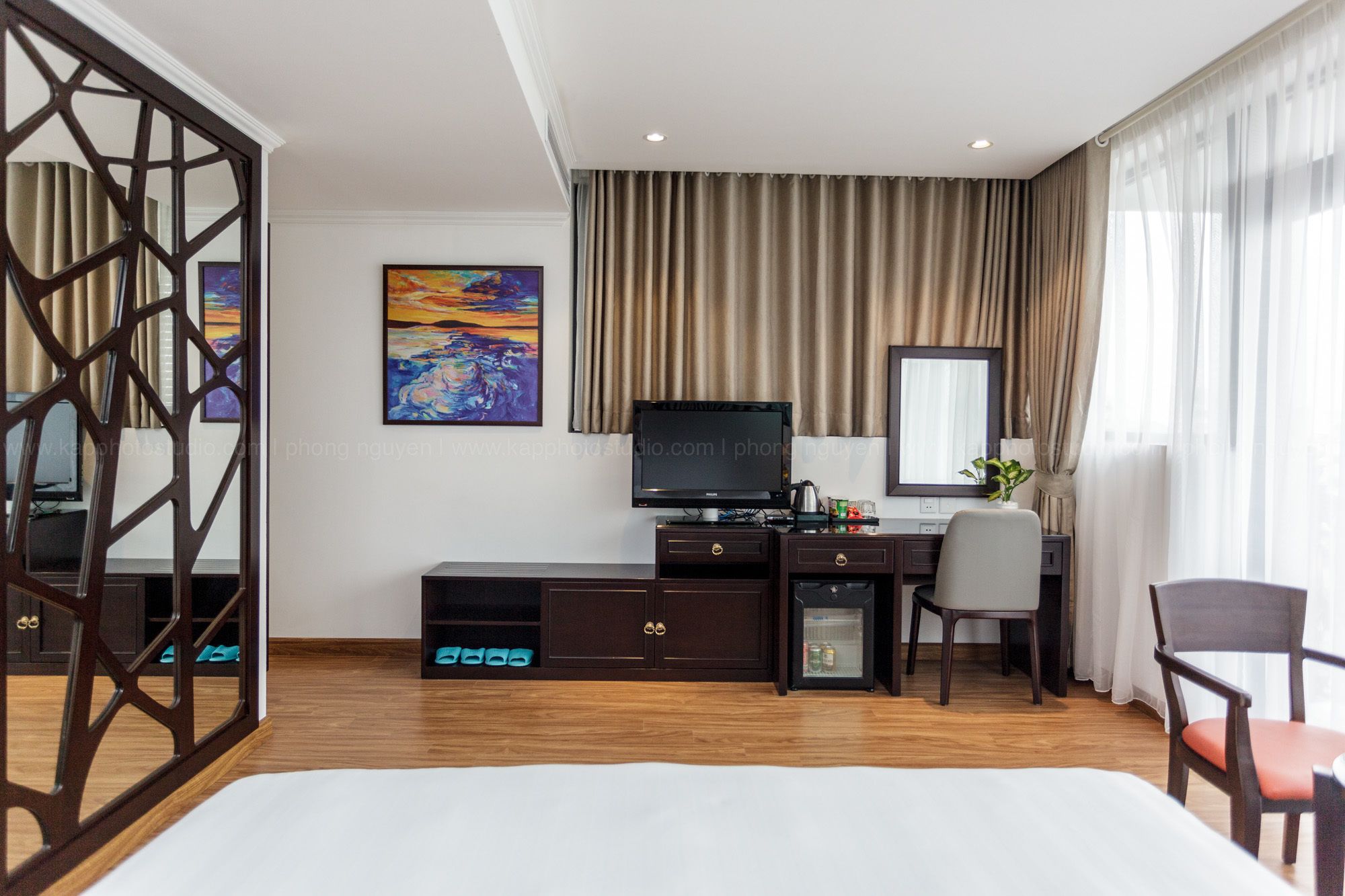 Een hotelkamer met een bed, een bureau met een computer, een stoel, een televisie en een schilderij aan de muur.