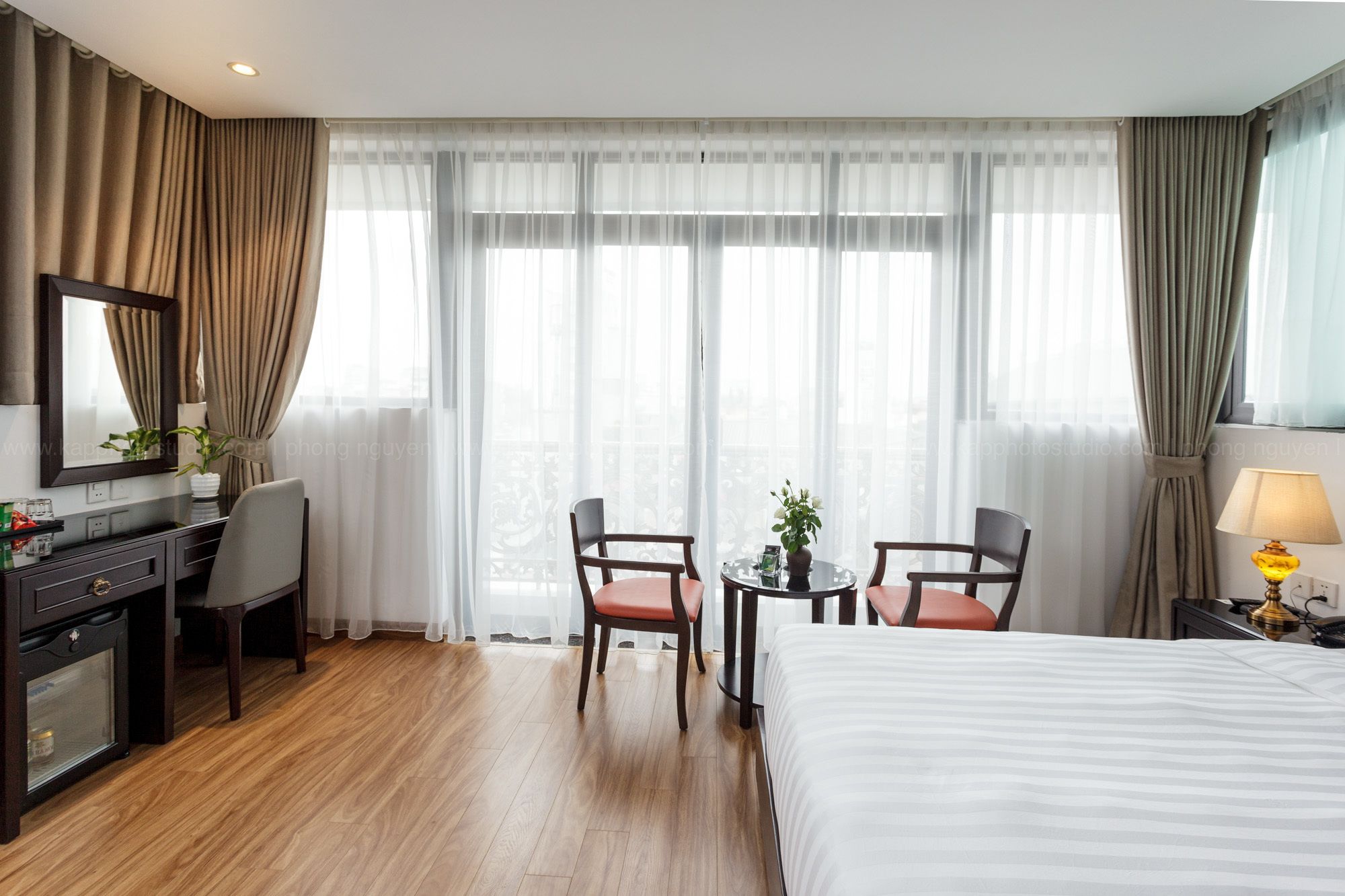Une chambre d’hôtel comprenant un lit, un bureau avec une chaise, deux chaises supplémentaires, une petite table avec une plante et une lampe.