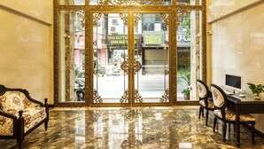 Un vestíbul amb sòl de marbre, portes daurades ornamentades i una zona de seients amb dues cadires i un escriptori.