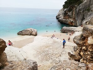 Une plage de galets avec une eau claire, des gens qui prennent des bains de soleil et quelques personnes qui se baignent.
