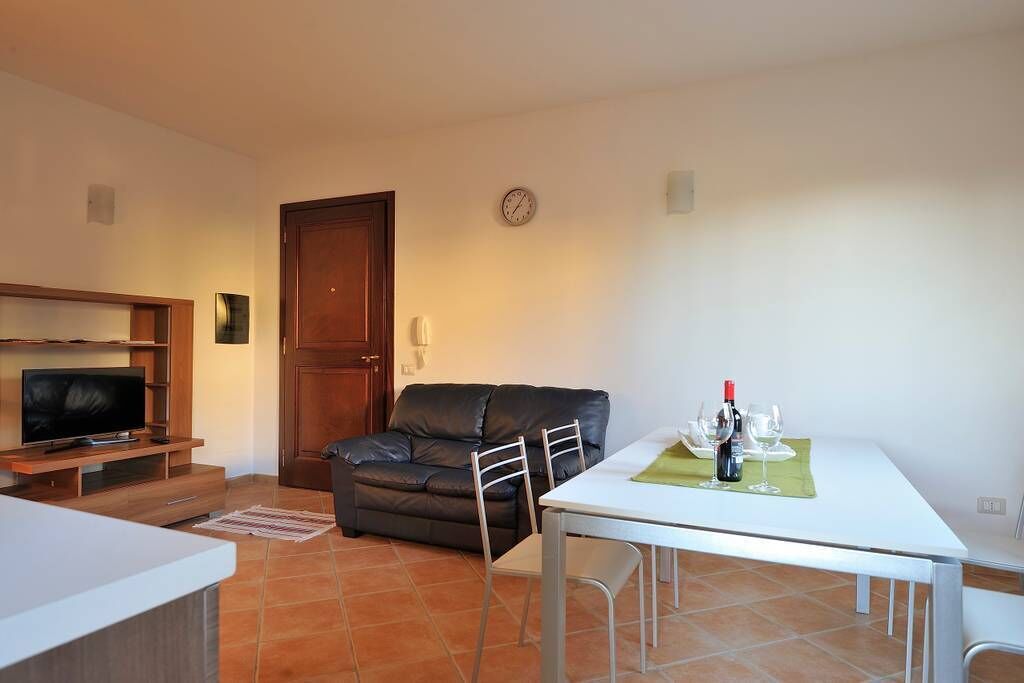 Un salon avec un téléviseur, un canapé en cuir, une table à manger avec des chaises et une horloge au mur.