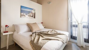 Een slaapkamer met een bed, nachtkastje, lamp, schilderij en een raam met gordijnen.