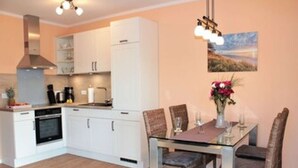 A modern kitchen with white cabinets, a built-in oven, and a dining area with a glass table and wicker chairs.