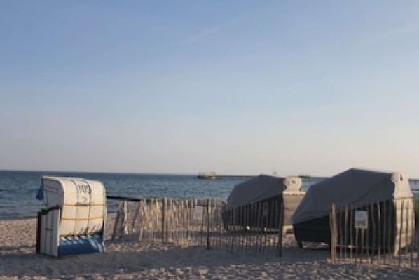 A beach with a wooden fence, a blue barrel, and a distant boat.