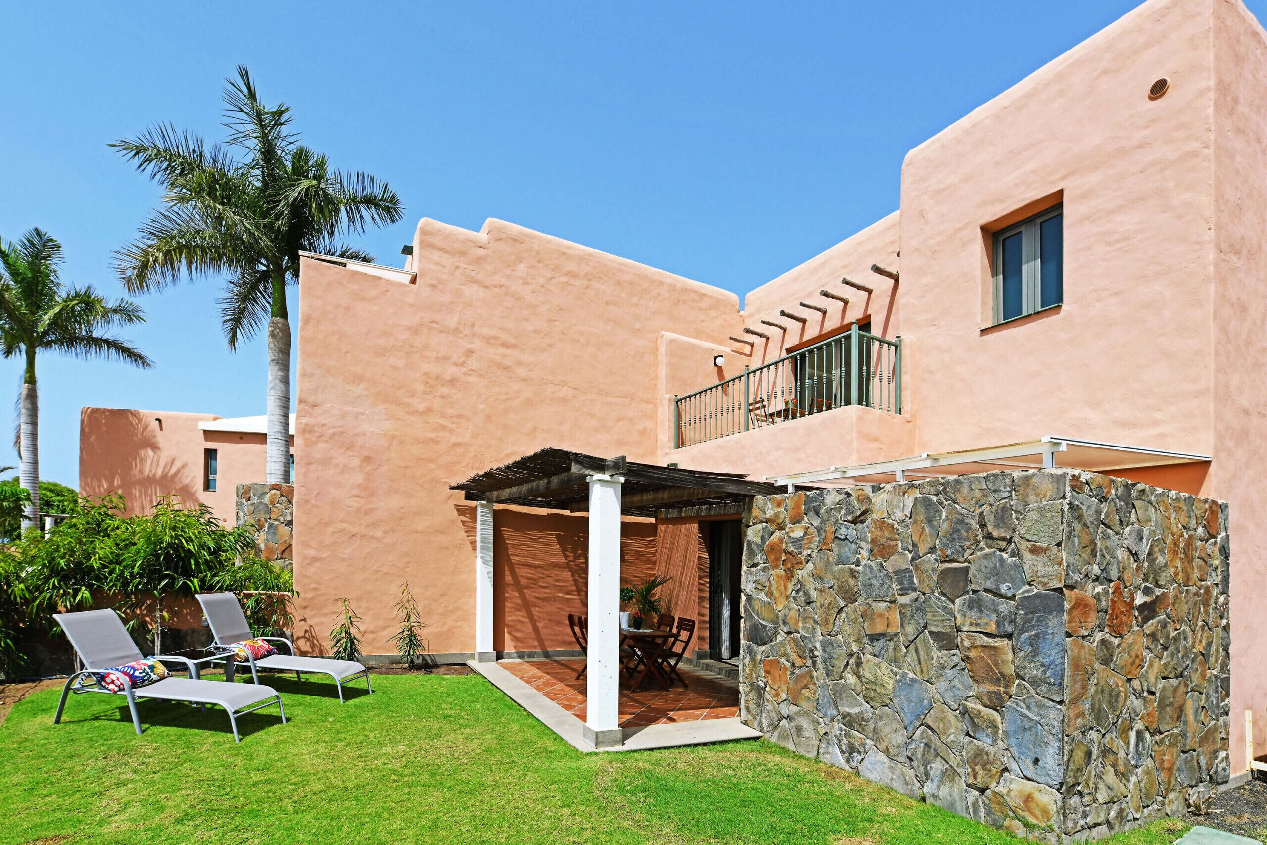 A building with a stone wall, a covered patio, and a pool area with lounge chairs.