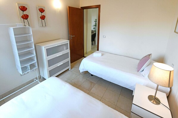 Een hotelkamer met twee bedden, een nachtkastje met lamp, een kledingkast en een spiegel.