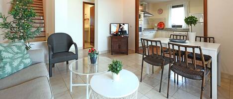 A modern living room with a sofa, a dining table with chairs, a small white table with a plant, and a staircase leading to another room.