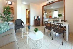 Ein modernes Wohnzimmer mit einer Couch, einem Esstisch mit Stühlen, einem kleinen weißen Tisch mit Pflanze und einer Treppe, die in einen anderen Raum führt.