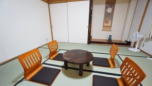 Une pièce avec un sol recouvert de tatamis, comprenant une table ronde et quatre chaises orange dotées de coussins noirs.