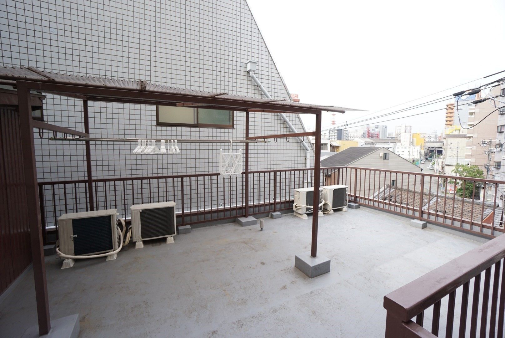 A rooftop terrace with a metal railing, two air conditioning units, and a small enclosed area with a window.