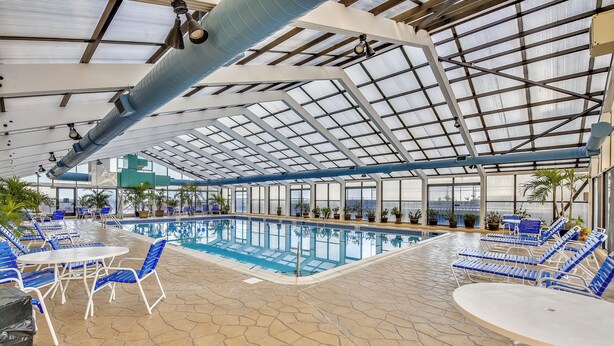 Ein Poolbereich im Innenbereich mit blauen Liegestühlen und Tischen, einem gefliesten Boden und einer Glaskuppel.