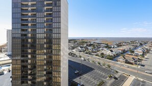 Un edificio de gran altura con varios pisos y balcones, con vistas a una ciudad costera con un puerto deportivo y zonas residenciales.