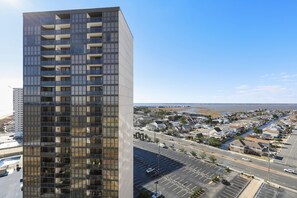 Un immeuble de grande hauteur, doté de nombreux étages et de balcons, qui offre une vue sur une ville côtière avec un port de plaisance et des quartiers résidentiels.