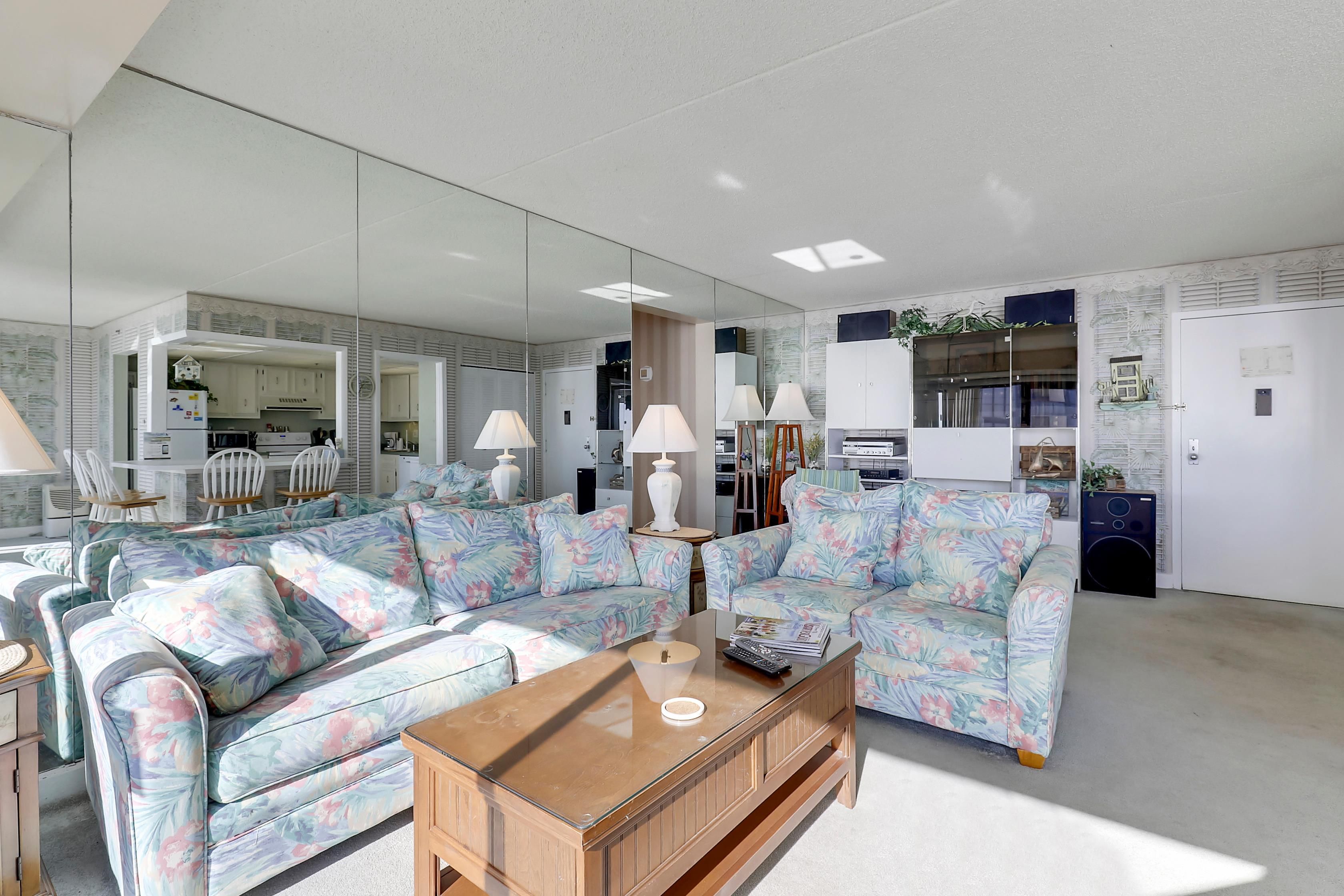 A modern living room with a sofa set, a coffee table, and a kitchen area visible through a glass partition.