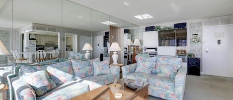 A modern living room with a sofa set, a coffee table, and a kitchen area visible through a glass partition.
