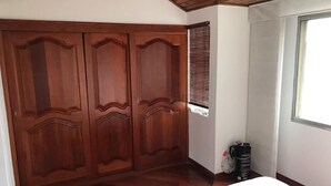 Una camera da letto con un armadio in legno, un letto con copriletto floreale e un termosifone, oltre a una finestra con persiane.