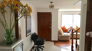 Un corridoio con una porta in legno, una sedia da ufficio nera, una vetrina in vetro e un vaso di fiori gialli.
