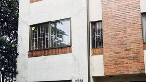 Edificio a più piani con facciata bianca e sezione in mattoni. Sono visibili finestre con grate e un portone.