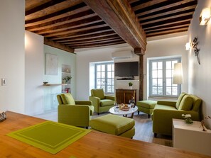 Un salon avec des canapés verts, une table à manger en bois et un téléviseur fixé au mur.