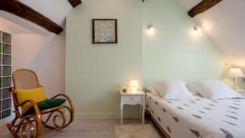 Een slaapkamer met een bed, een schommelstoel, een nachtkastje en een aan de muur hangend schilderij.