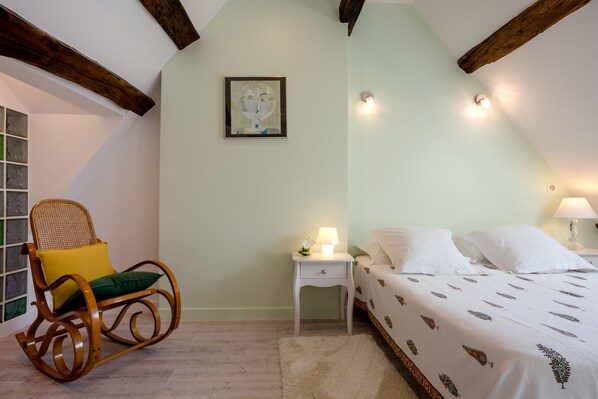 A bedroom with a bed, a rocking chair, a nightstand, and a wall-mounted picture.