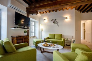 Un salon avec un canapé vert, un téléviseur à écran plat et une table à manger où sont disposés des plats et des boissons.