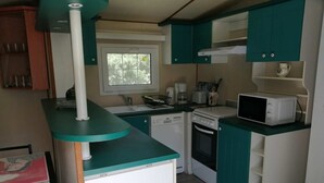 Une cuisine compacte avec des meubles de couleur turquoise, un lave-vaisselle, un four, un four à micro-ondes et une fenêtre donnant sur les arbres.