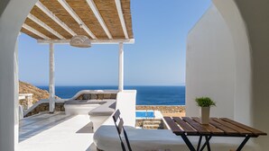 A covered outdoor seating area with a view of the sea, stone steps, and a wooden table. - Mykonos Unique Villas (Mykonos)