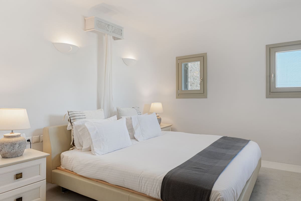 A bedroom with a bed, bedside tables, lamps, a window, and a wall-mounted light fixture.