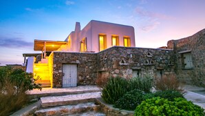 A modern house with a stone facade, a wooden deck, and a staircase leading to the entrance. - Mykonos Unique Villas (Mykonos)