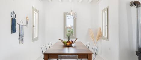 Une salle à manger avec une table en bois, des chaises transparentes, un panier de fruits et des éléments décoratifs accrochés au mur.