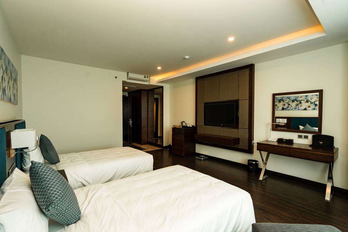 A hotel room with two beds, a desk, a TV, and a painting.