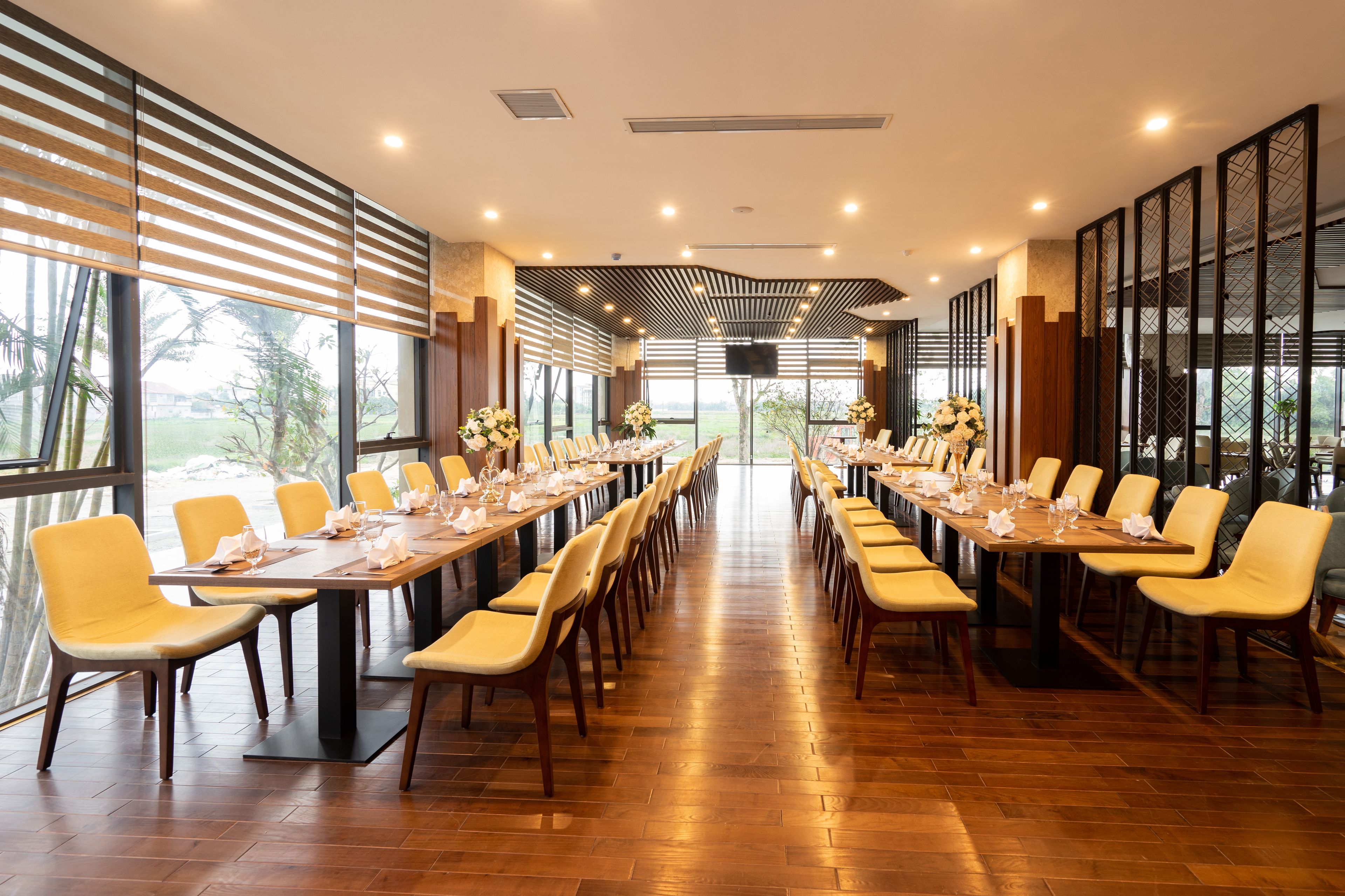 Una larga mesa de comedor con sillas, ventanas amplias y vistas a la vegetación.