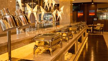 En buffetopstilling med rustfrie serveringsfade og en moderne lysekrone.