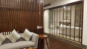 Uma sala de estar moderna com um sofá, almofadas listradas, uma pequena mesa de madeira e vista através de uma porta de vidro com persianas de metal.