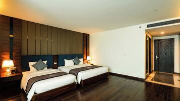 A hotel room with two beds, wooden headboard, dark flooring, and a door with a dark panel.