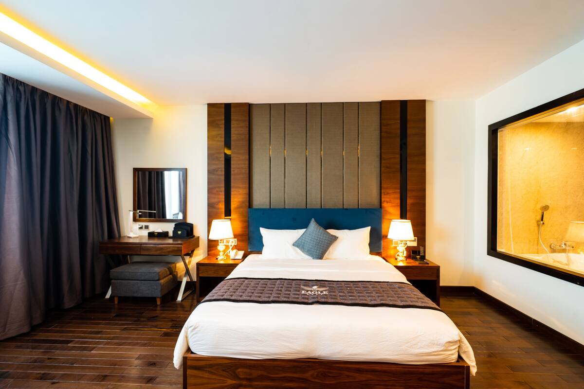 A hotel room with a large bed, a desk, a chair, a mirror, and a window.