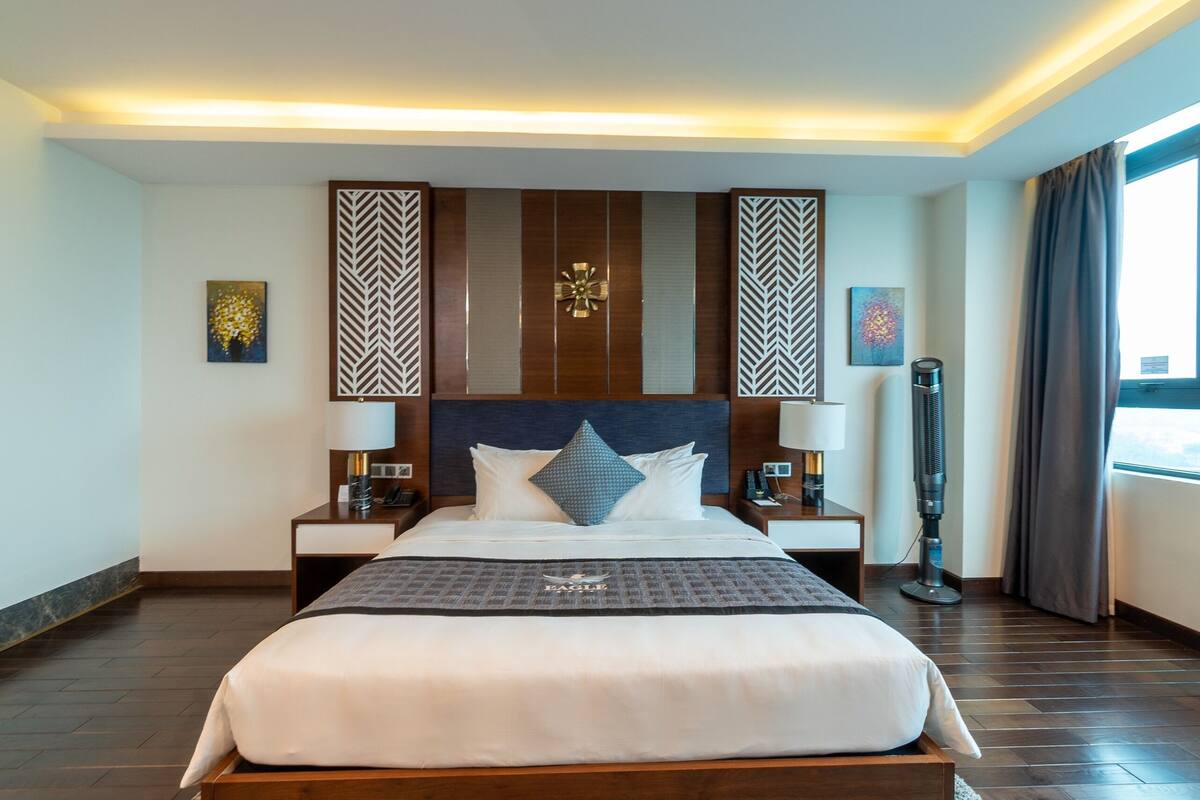 A hotel room with a large bed, two bedside tables, a floor lamp, and a window with curtains.