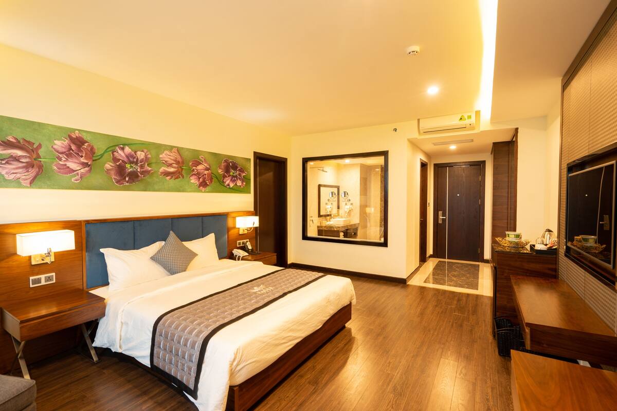 A hotel room with a large bed, bedside tables, a mirror, and a wall-mounted artwork.
