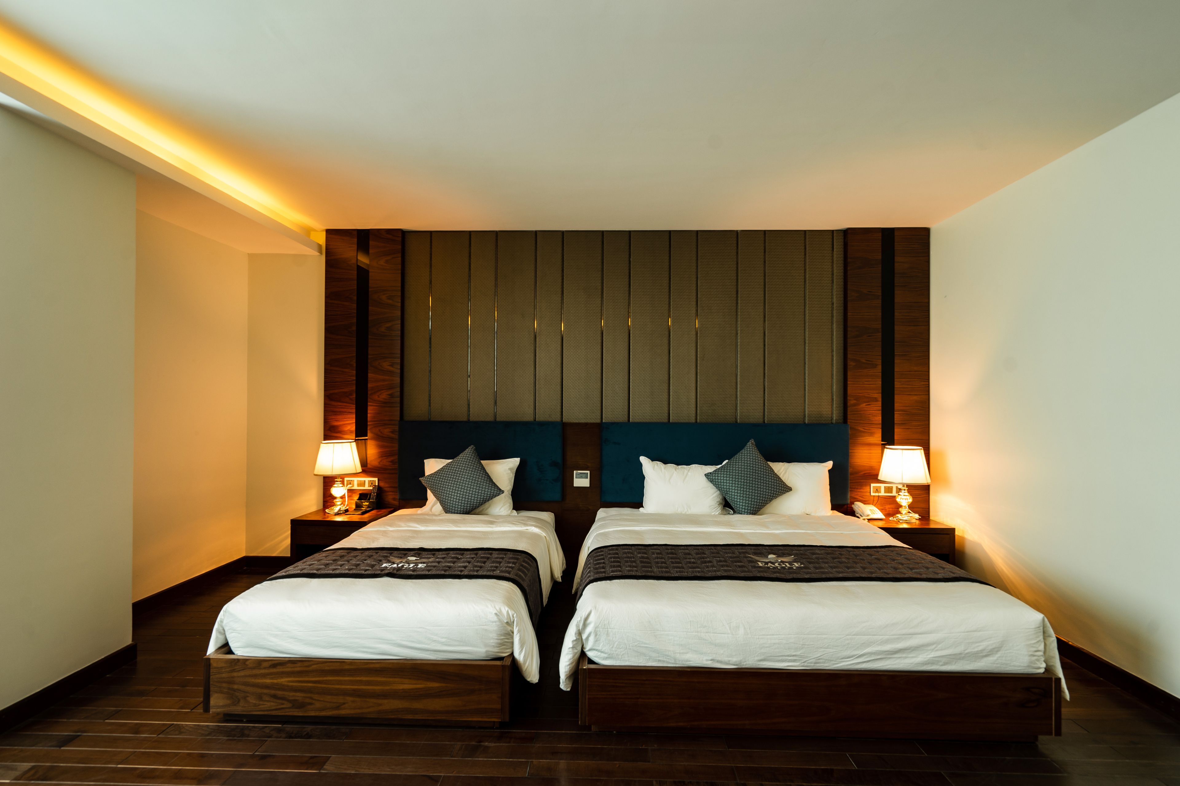 Habitación doble con dos camas, cabecera de madera, lámparas de noche y suelo de madera.